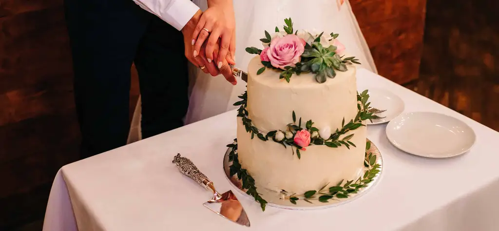Novomanželé krájí klasický dvoupatrový svatební dort s květinovou dekorací.
